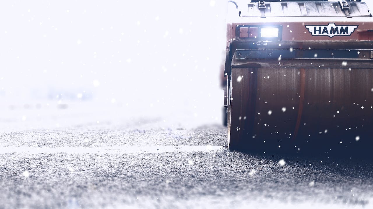 Close-up of a road roller working on an icy highway during heavy snowfall.