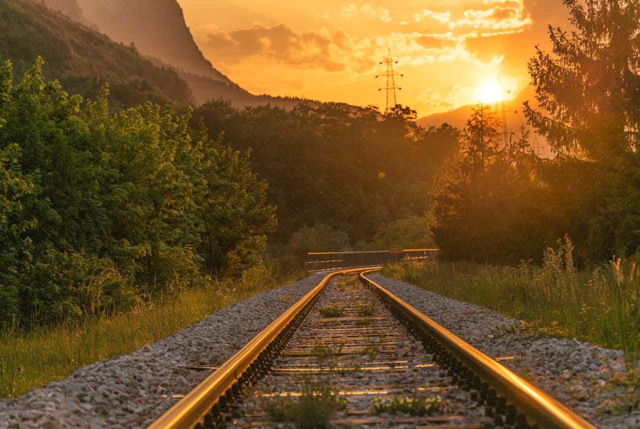 The Art of Drawing Readers In: Your attractive post title goes here Golden sunset over railway tracks surrounded by lush greenery and mountains.